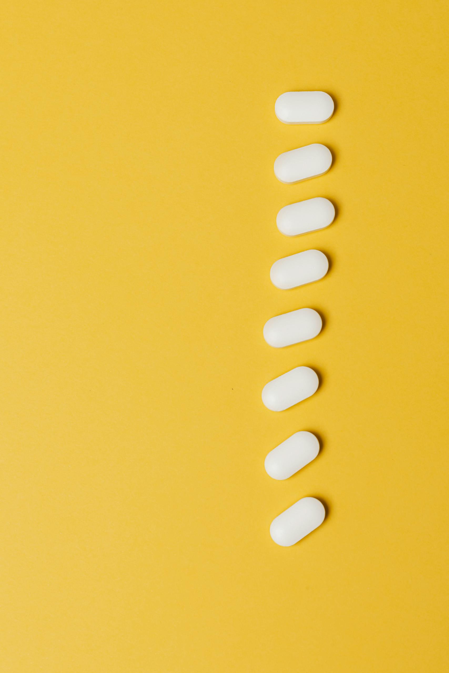 Top view composition of white medical pills placed in row vertically on vivid yellow background